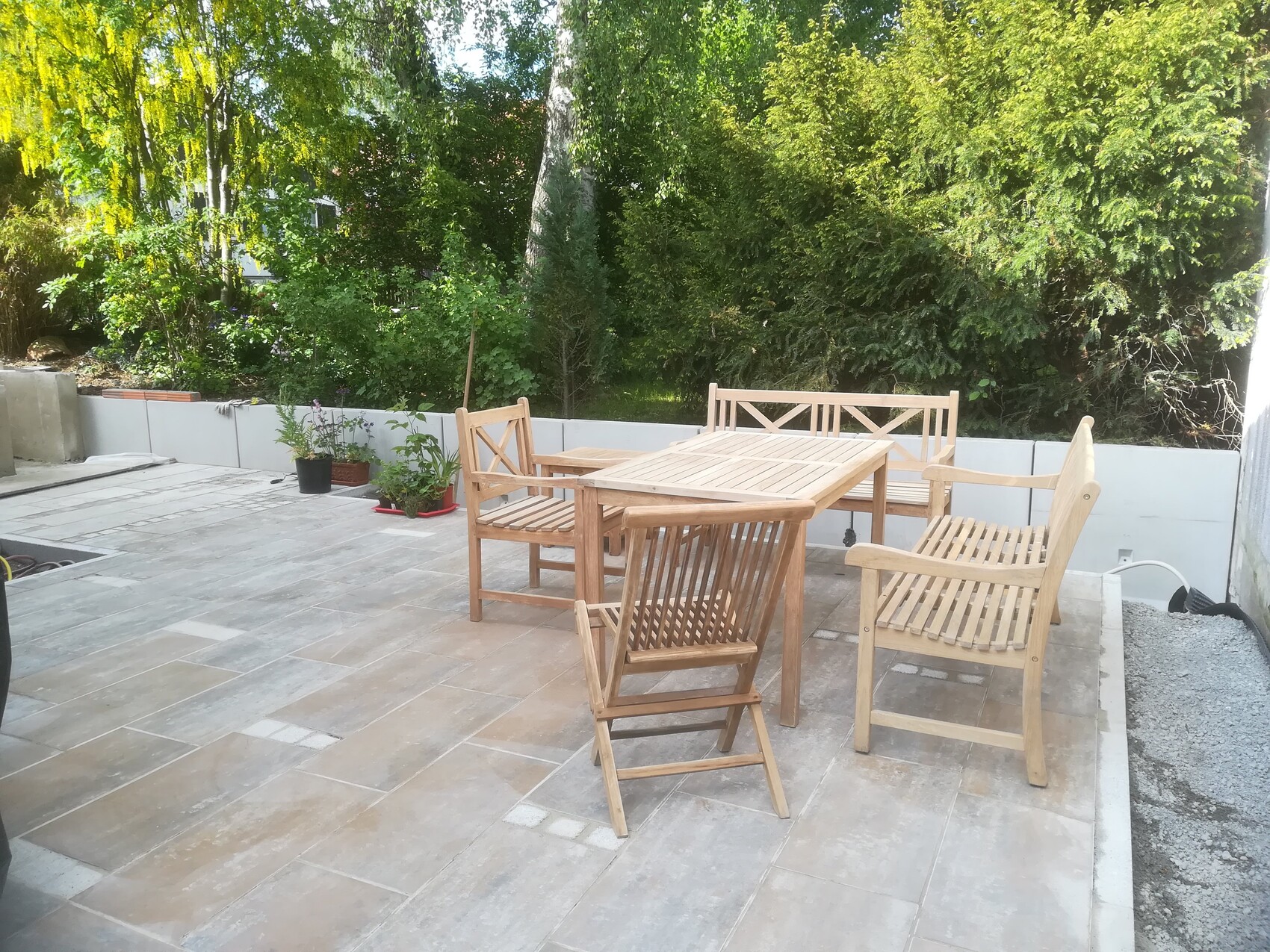 Garden patio with wooden table and chairs on terrace slab, green hedges in the background.