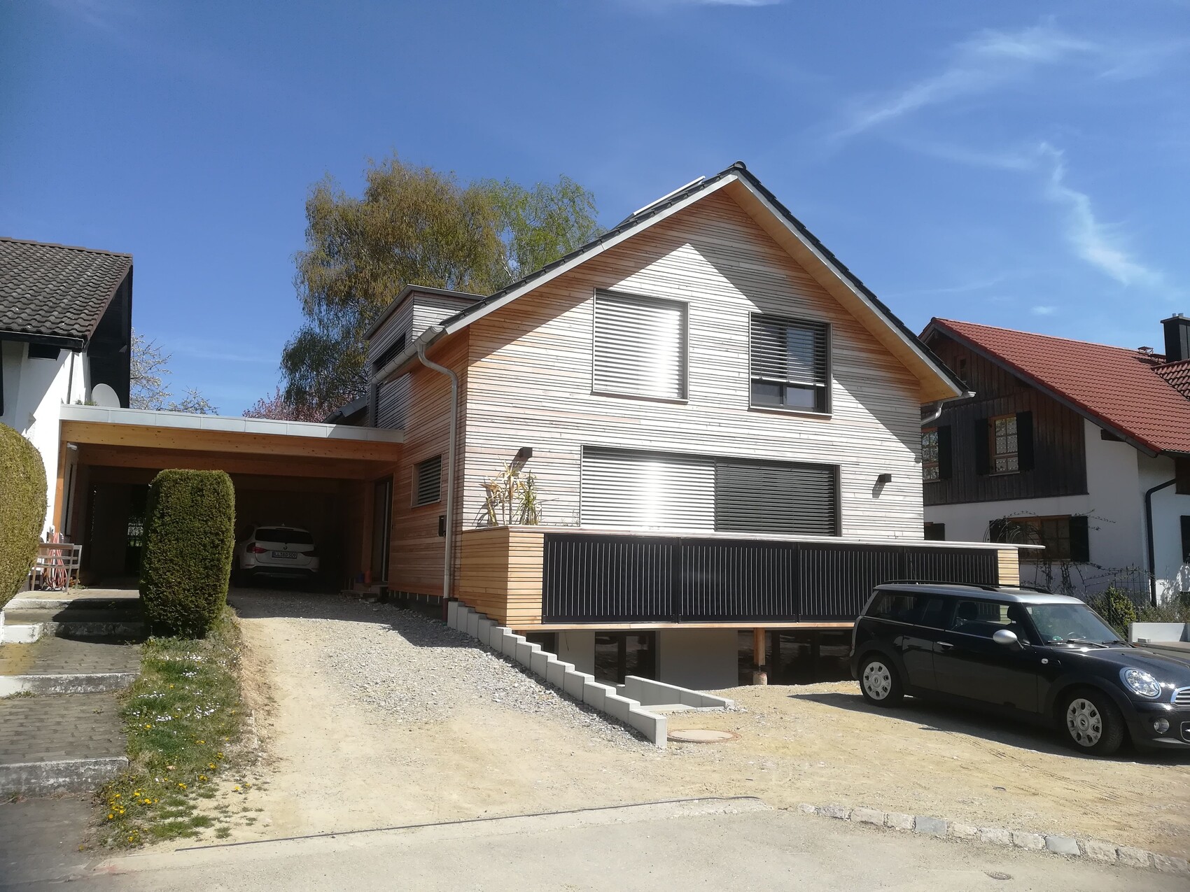 Modern house with wood cladding, carport on the left with car, blue sky above.