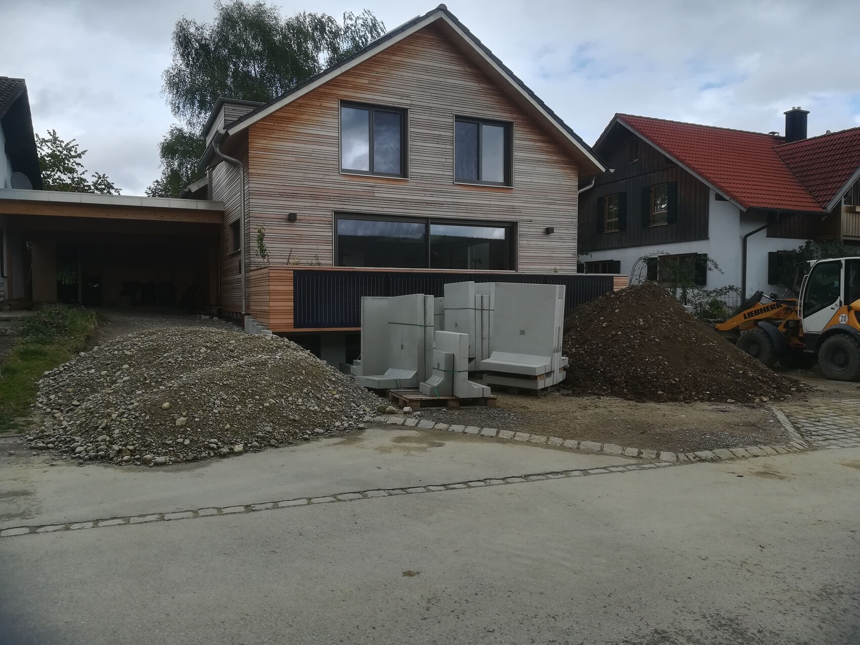 Construction site in front of a wooden house: pile of gravel, concrete slabs, construction machine.