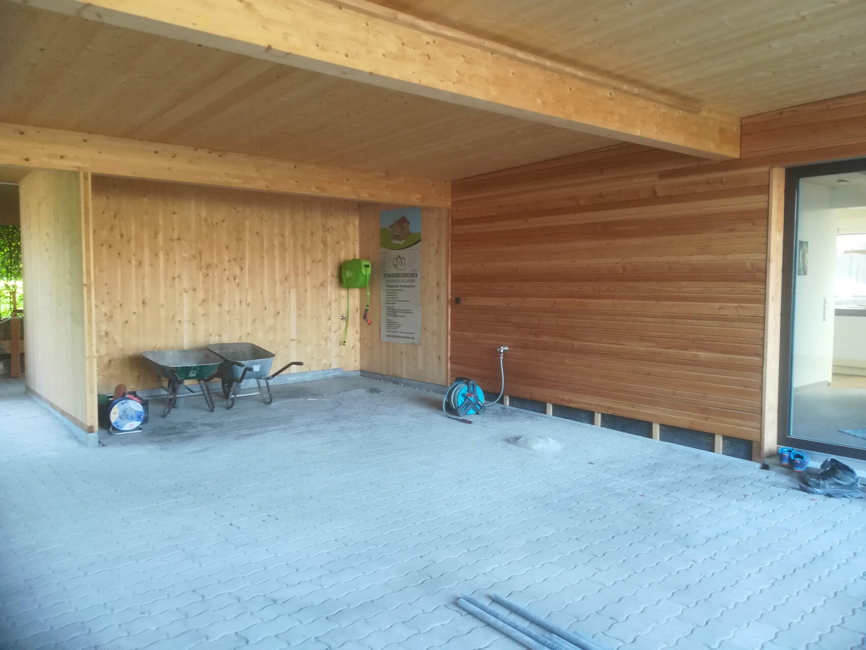 Open construction area with wooden walls, two wheelbarrows, hose reel and info board.