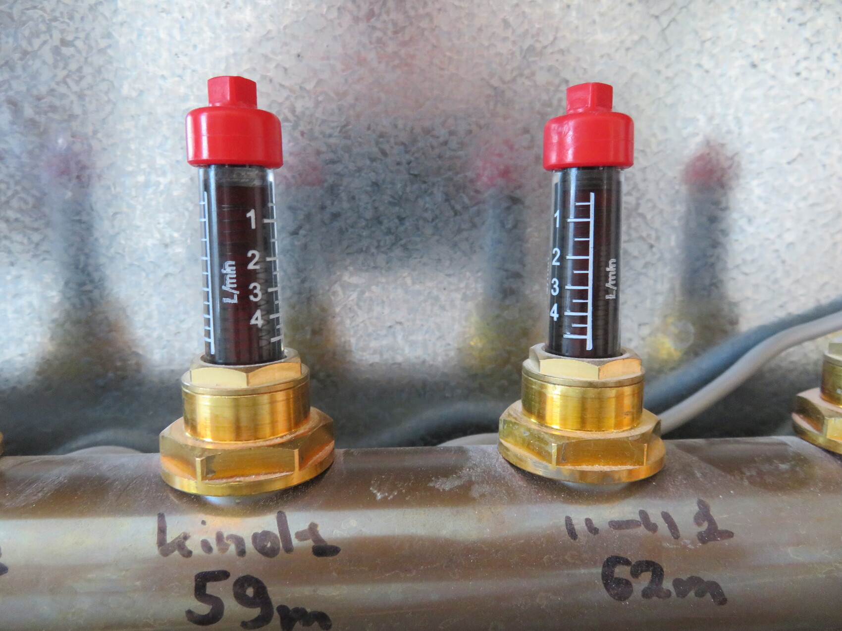 Two flow meters with red caps on a metal pipe; scale shows L/min.