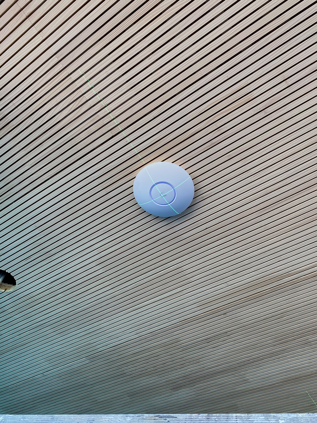 Round LED puck light on a ribbed ceiling with diagonal lines.