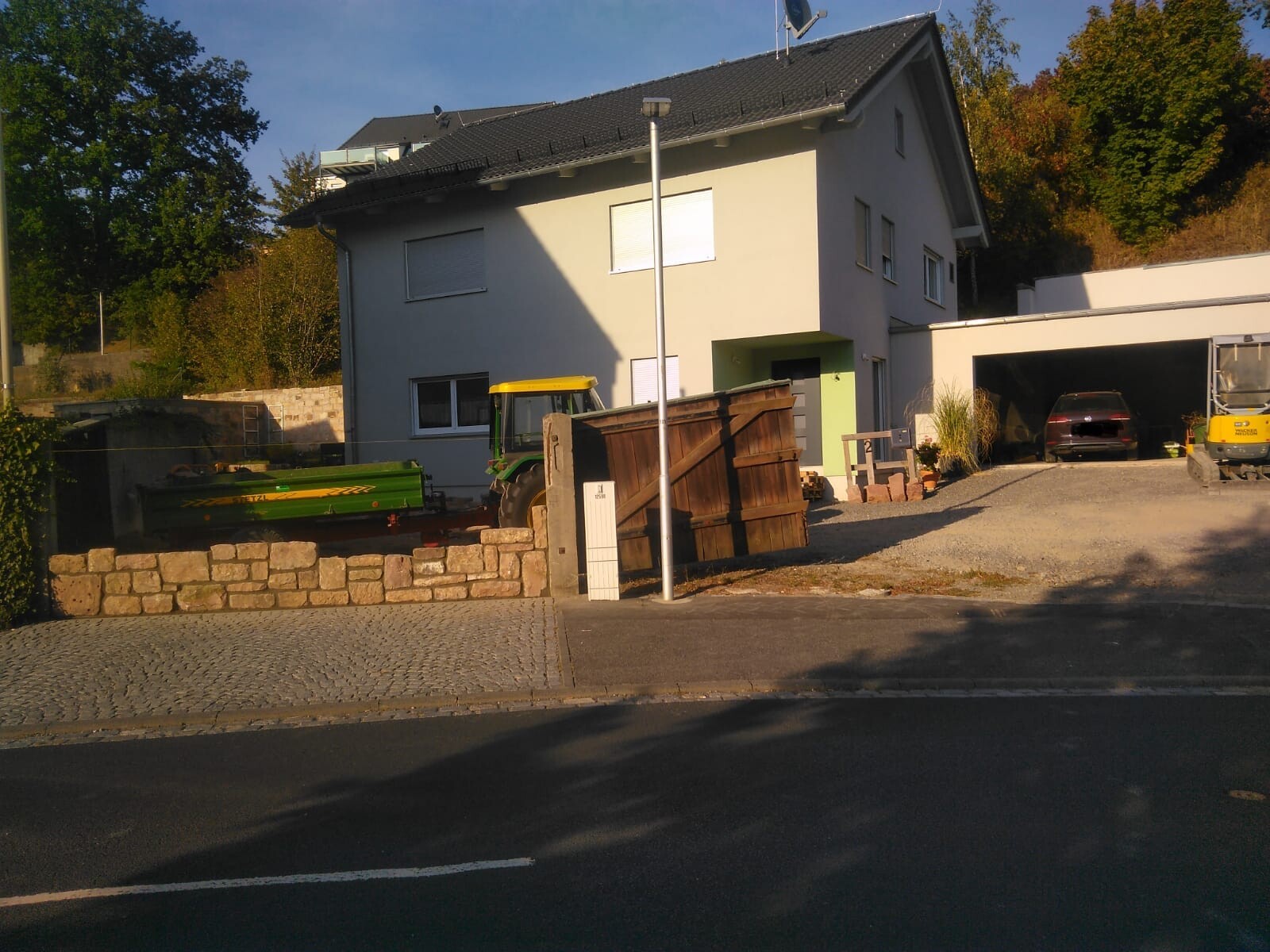 Residential building with courtyard, tractor, wood pile, and garage with car in the background.