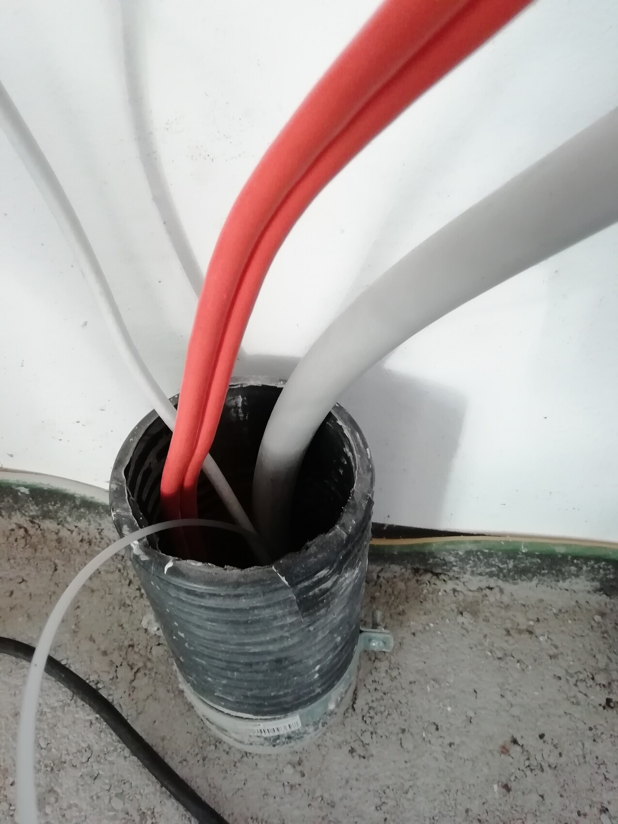 Multiple cables (red and gray) leading into an open black conduit on the ground at the construction site.