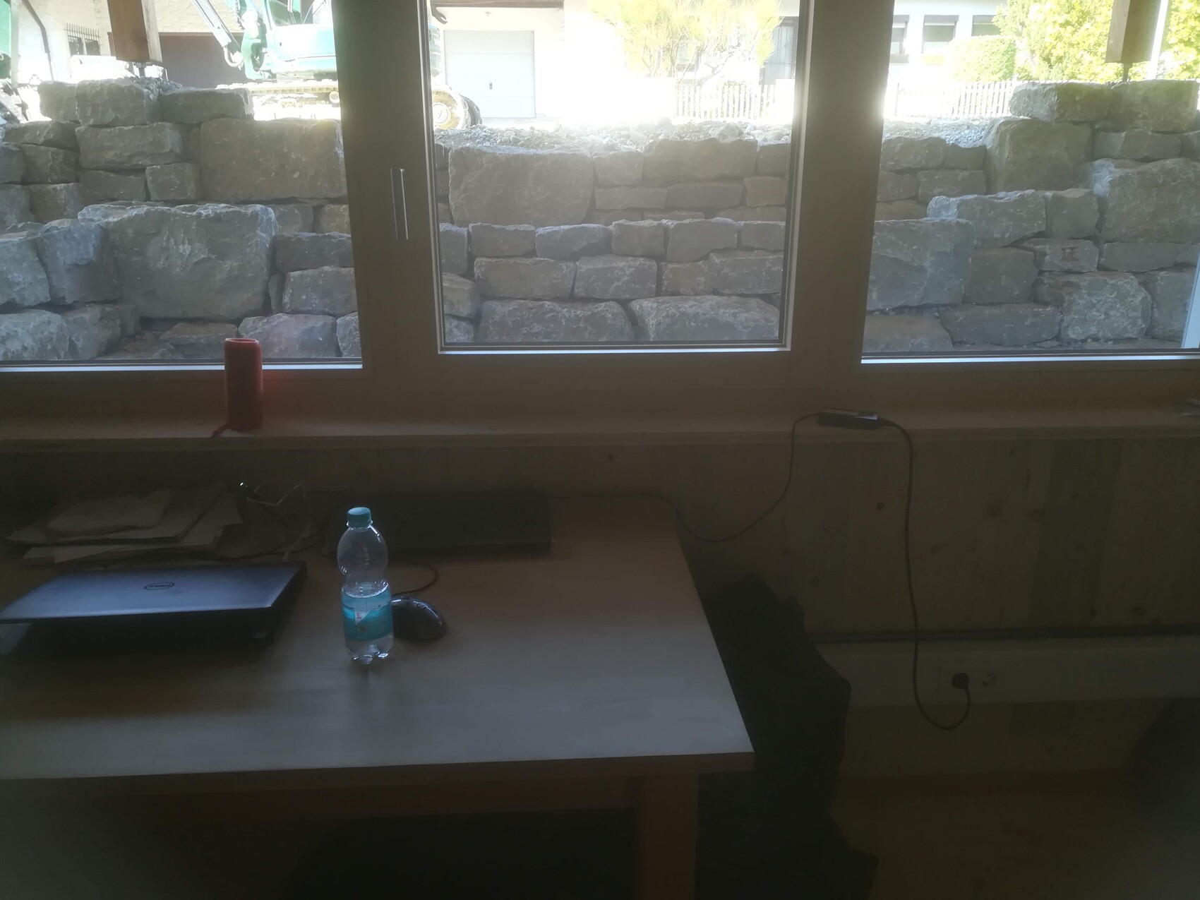 Workspace by window with laptop, water bottle, mouse and red candle; outside a stone wall.