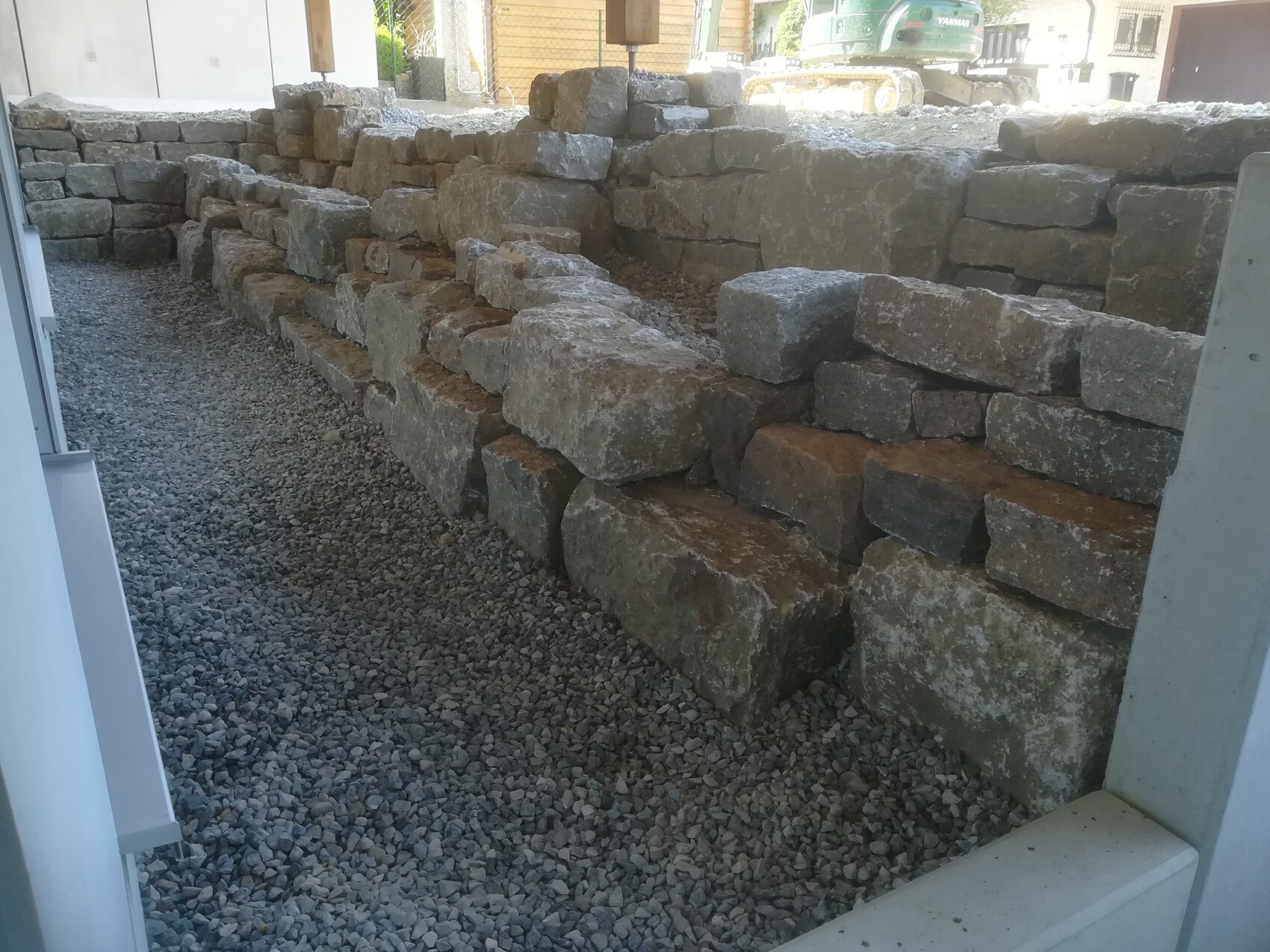 Massive stone wall being built on a construction site, gravel ground in front.