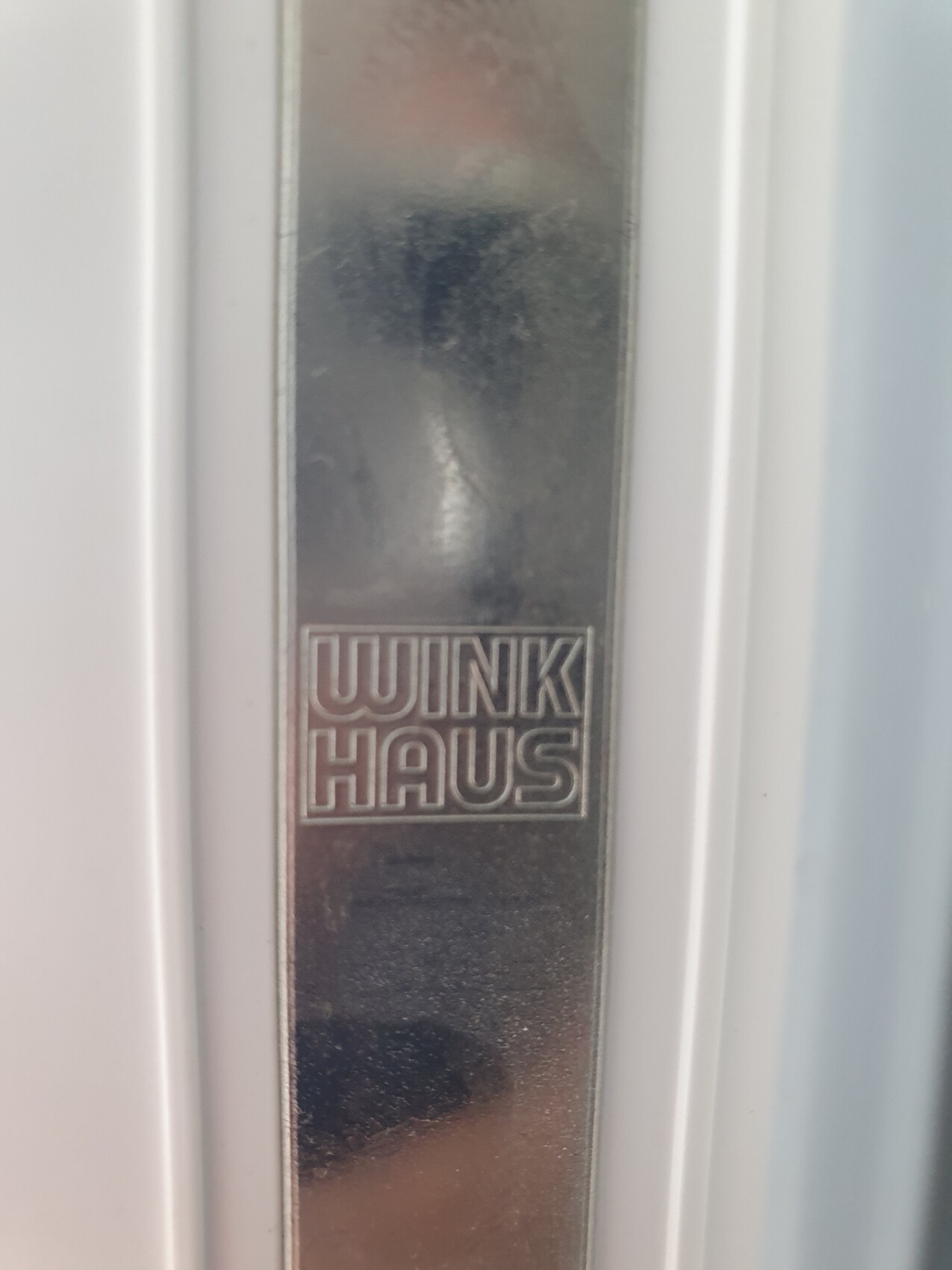 Close-up of a metal door frame strip with engraved WINKI HAUS logo.