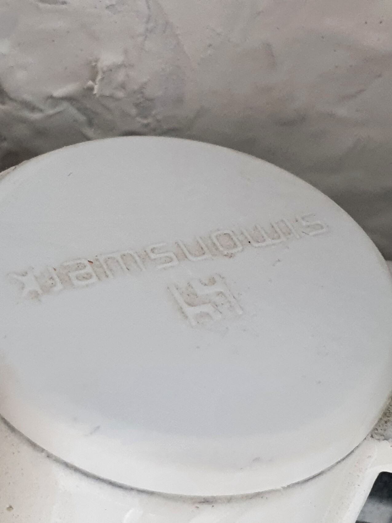 White round plastic cap with embossed lettering in front of rough wall.