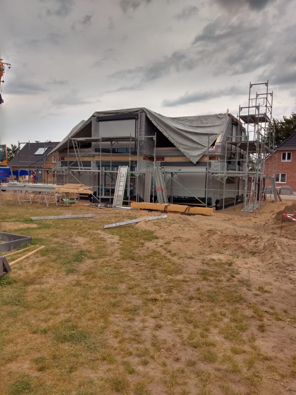Baustelle mit unfertigem Haus, Gerüst, Planen, Holzbalken und Baumaterialien.