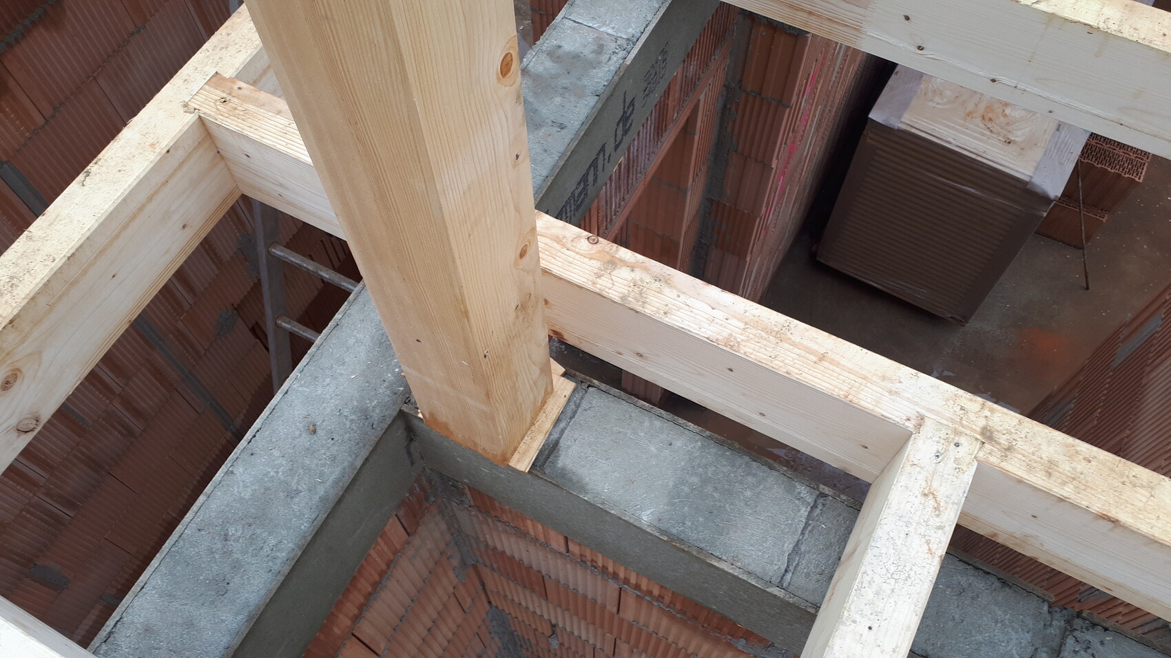Ansicht eines Rohbaus: Holzrahmenkonstruktion über Betonboden, Ziegelwände im Hintergrund.