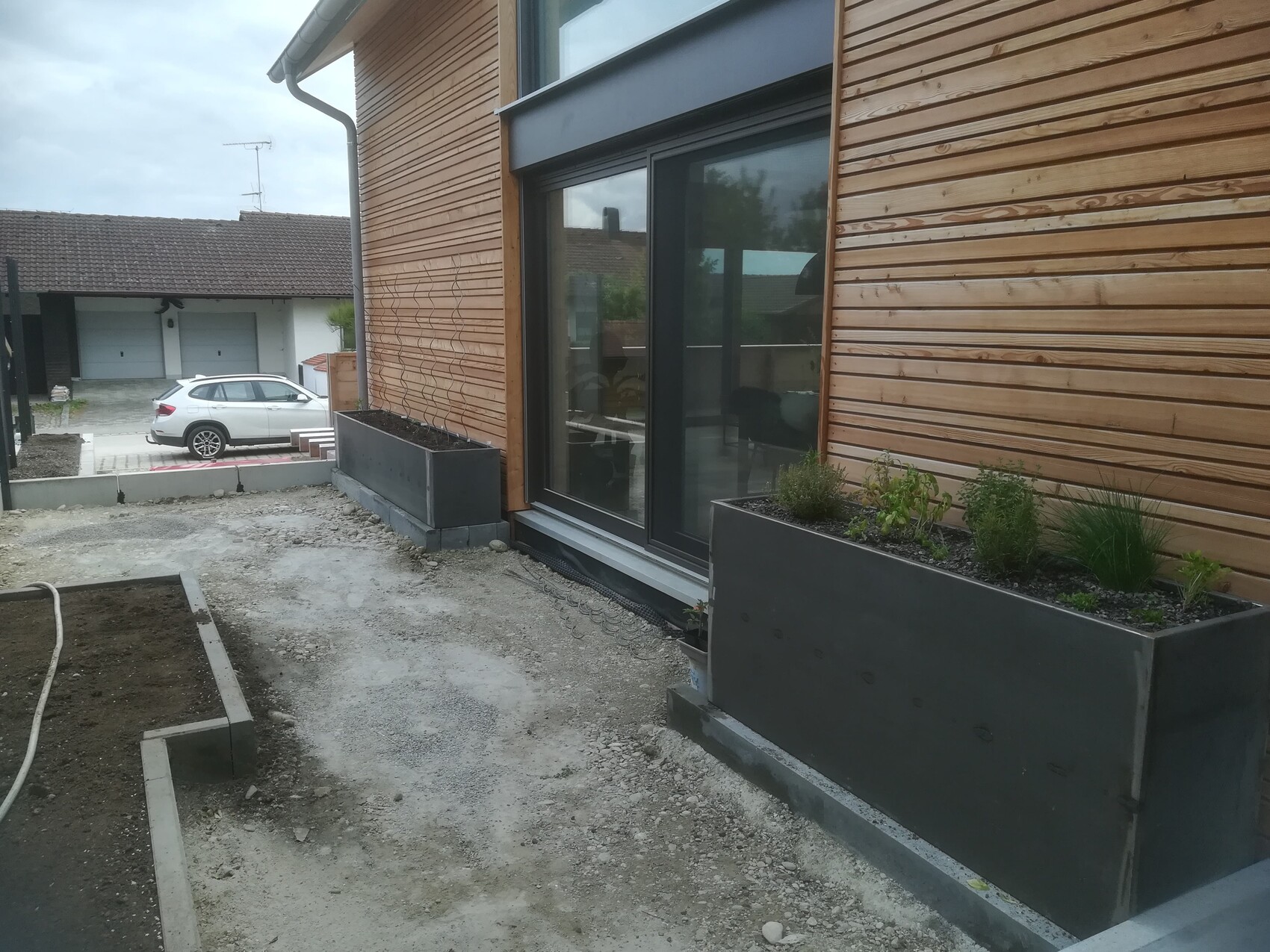 Modern wooden facade with large glass windows and rectangular metal planter boxes with plants.