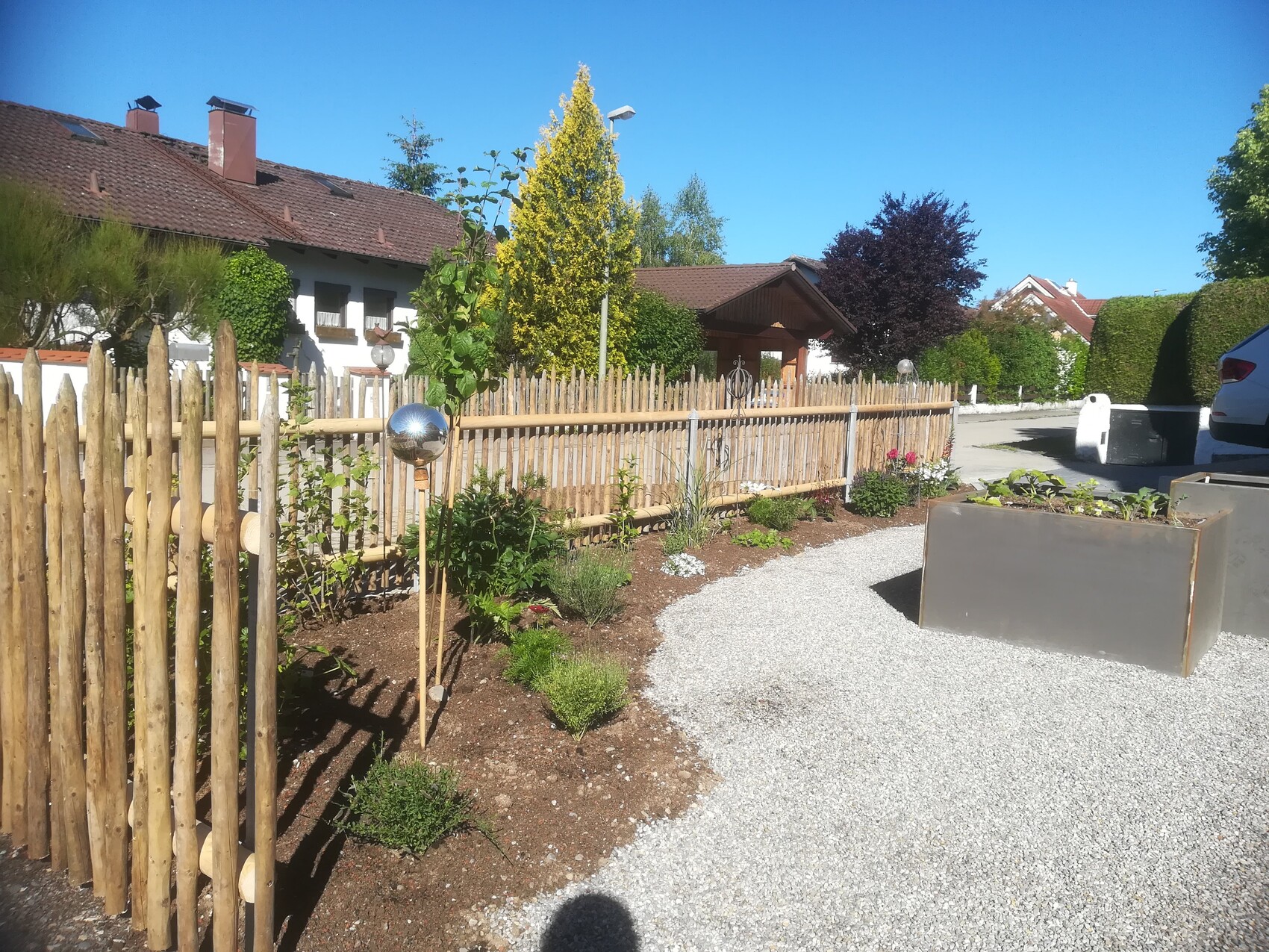 Garden with wooden fence, gravel path, planter boxes, and house in the background