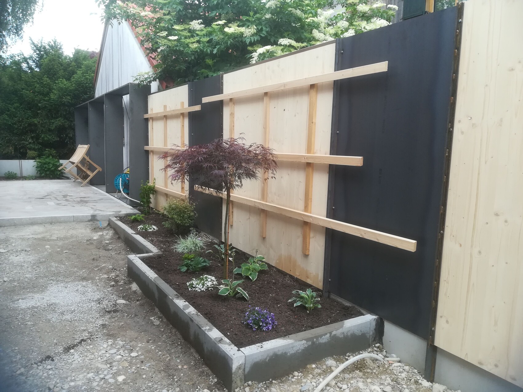 Garden with temporary slatted fence, planting bed, and deck chair in the background.