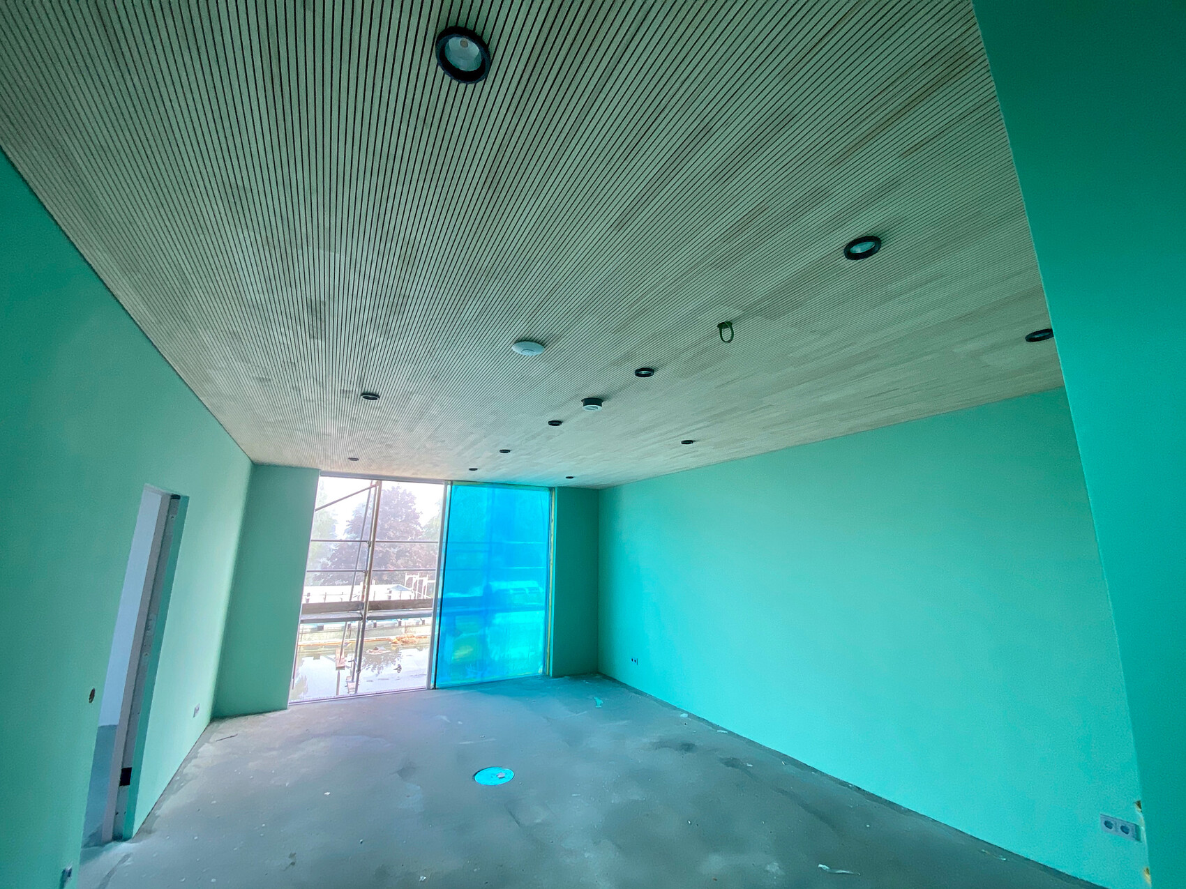Unfinished interior with mint green walls, striped ceiling, and large windows.
