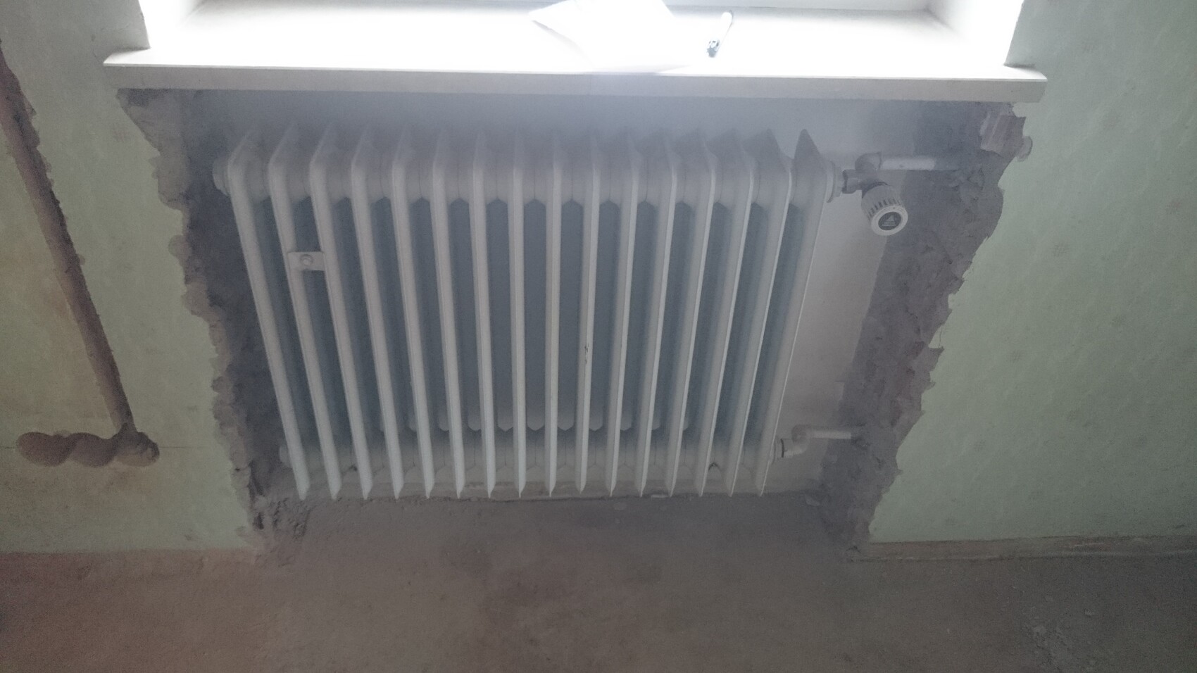 White radiator with vertical tubes in front of raw wall plaster; visible renovation work.