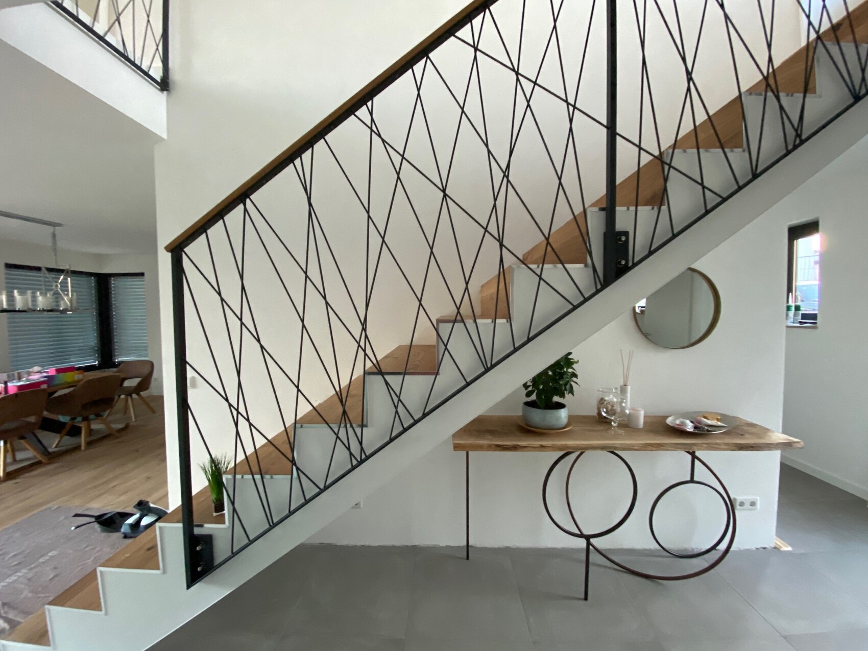 Modern staircase with black wire railing, wooden steps, table with plant and round mirror