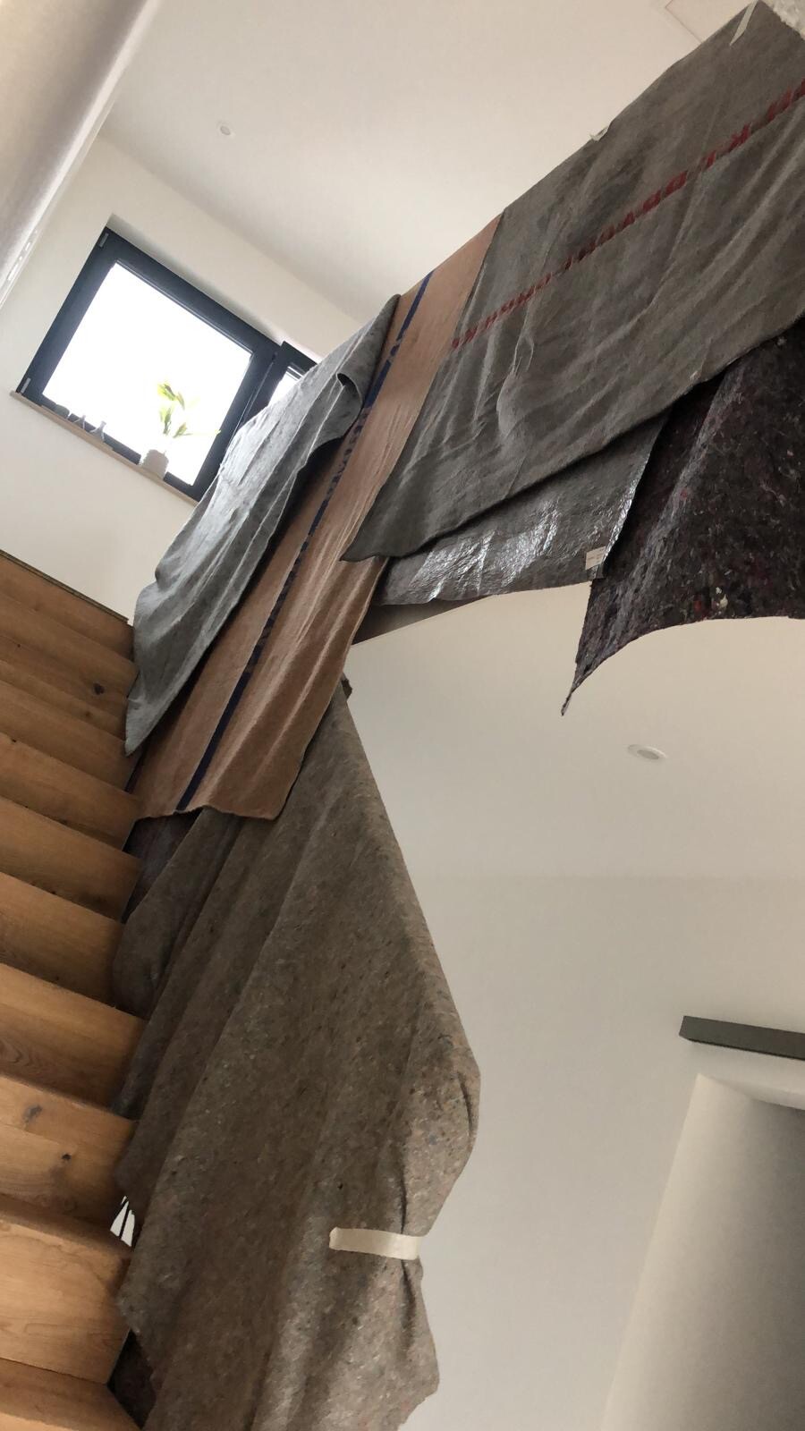 Wooden staircase with large gray protective sheets hanging over the steps; window with plant visible.