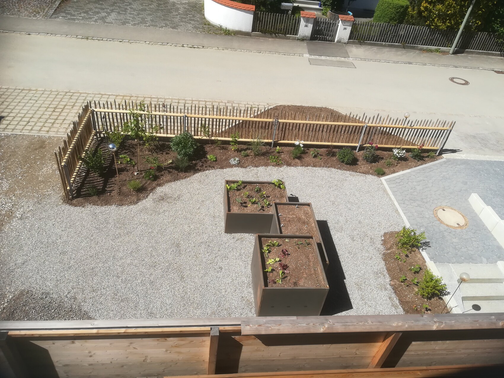 Garden area behind a wooden fence with three square planter boxes and gravel surfaces.
