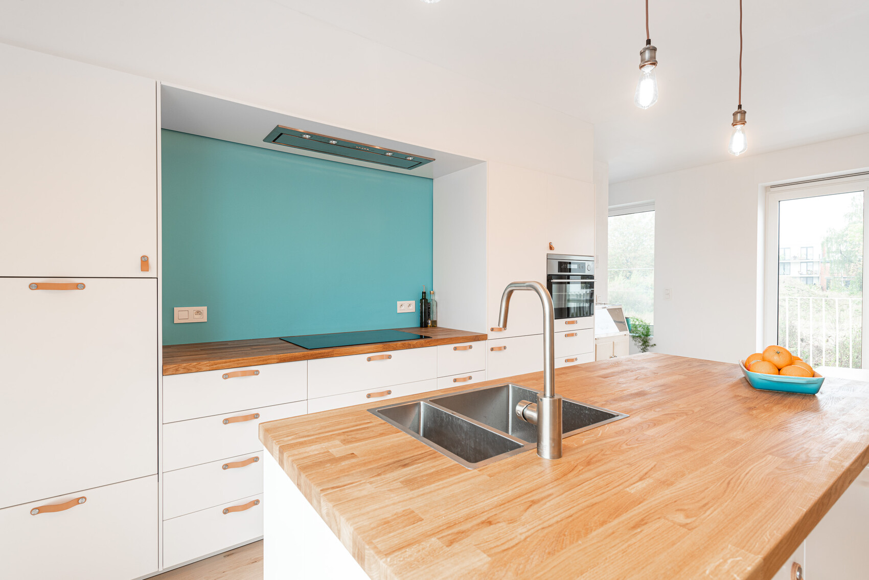 Modern kitchen with white cabinets, turquoise backsplash, and wooden island with sink.