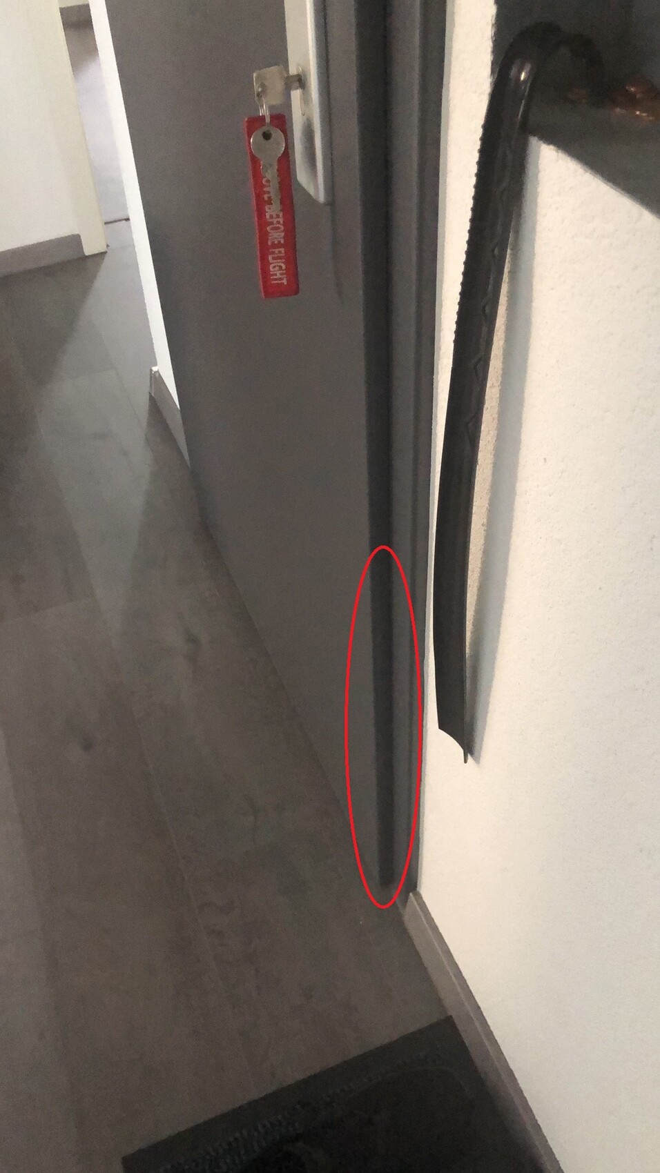 Close-up view near the floor of a gray door with a red keychain on the handle; narrow gap between door and frame.