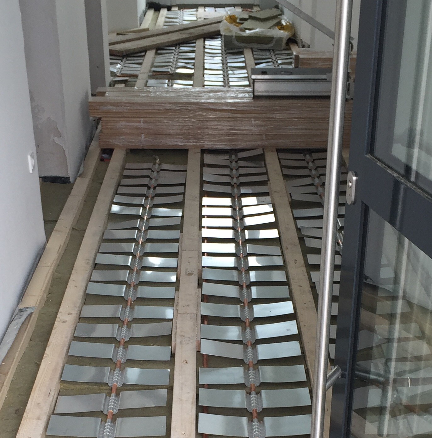 Interior of a construction site: wooden battens lie on the floor, metal slats in rows, door on the right.