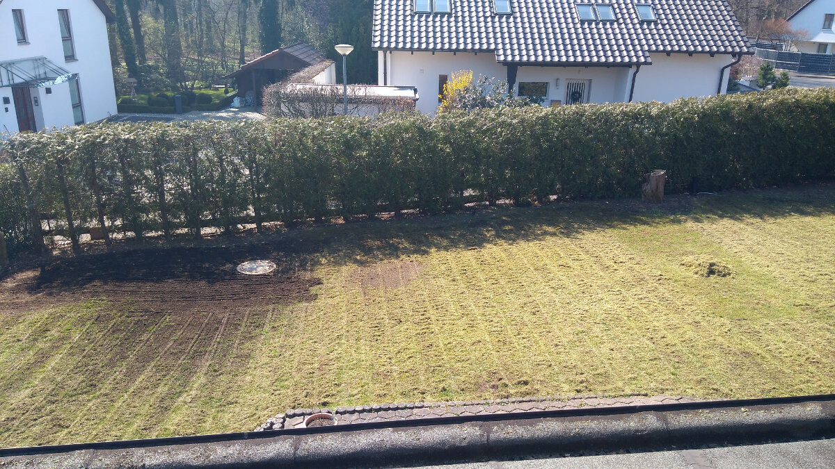 Garden view: mowed lawn, dense hedge, white houses with tiled roofs in the background.