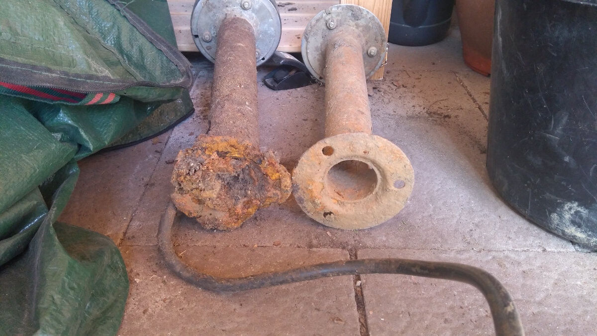 Two rusty pipe pieces with flanges lie on the ground; one heavily rusted, indoors.