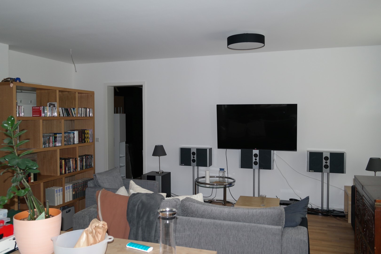 Living room with large-screen TV on white wall, surround sound system, sofa, and bookshelf.