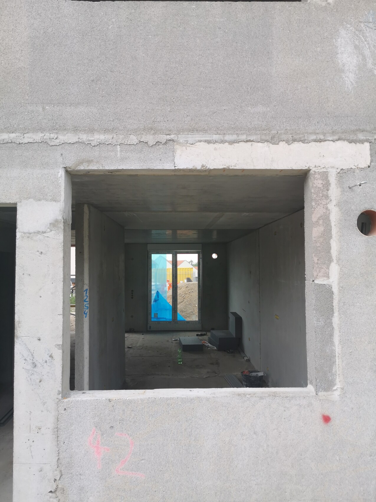 Unfinished concrete shell: interior with window opening, view of exterior with building materials.