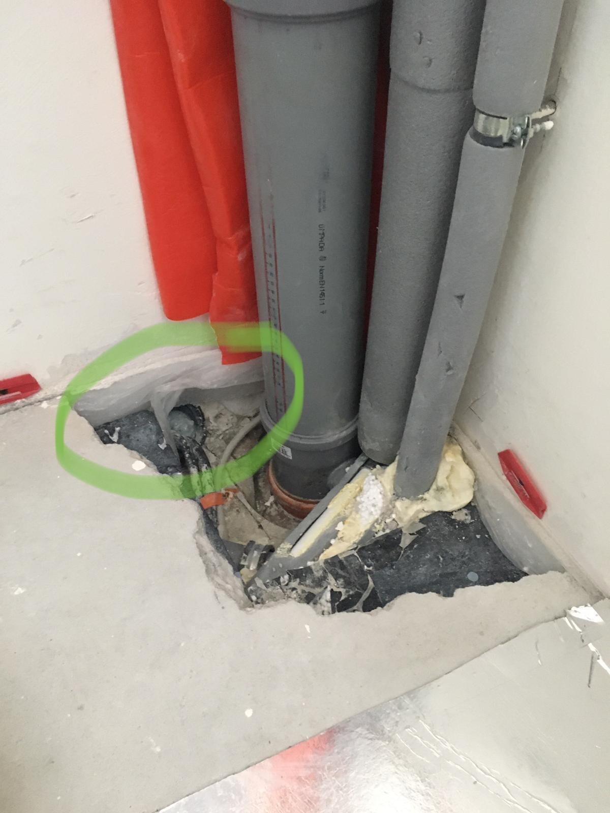 Open pipes in red and gray, floor break, exposed cables and insulation material.