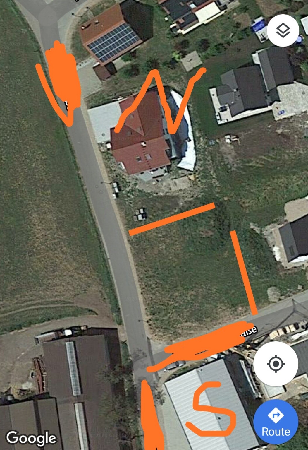 Satellite image of a residential area with red roofs, streets and orange markings on the site.