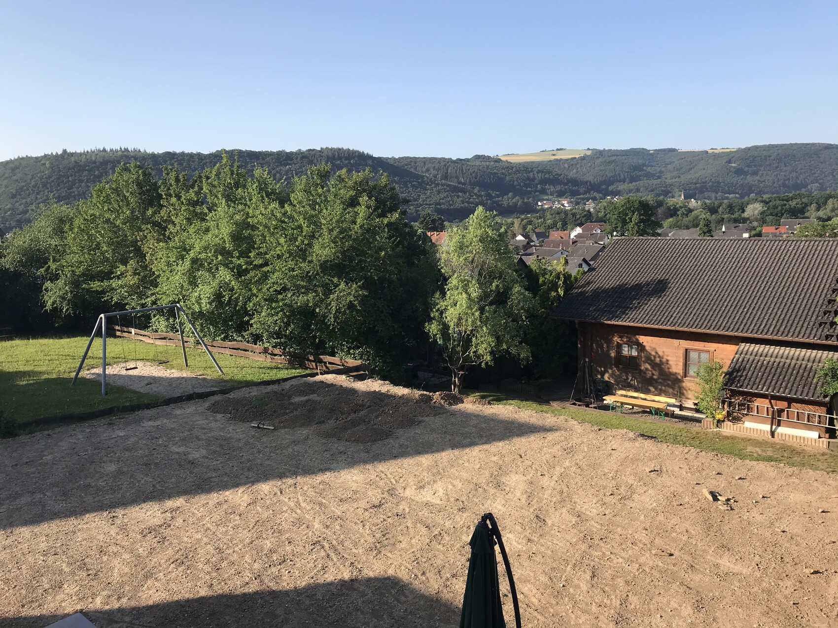 Hügellandschaft mit Haus, Bäumen und Spielplatz im Gartenbereich