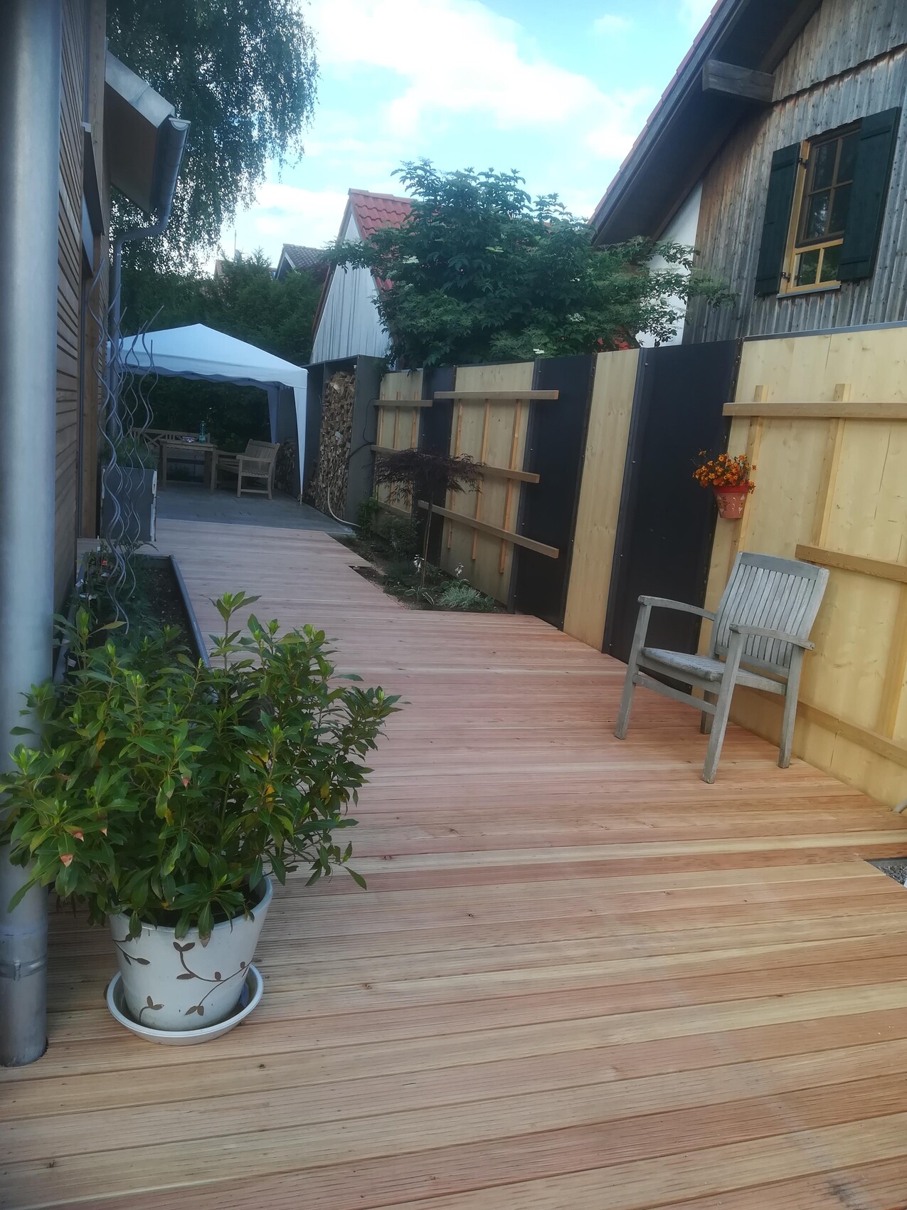 Wooden deck garden path with planter on the left, chair on the right, wooden wall in the background.