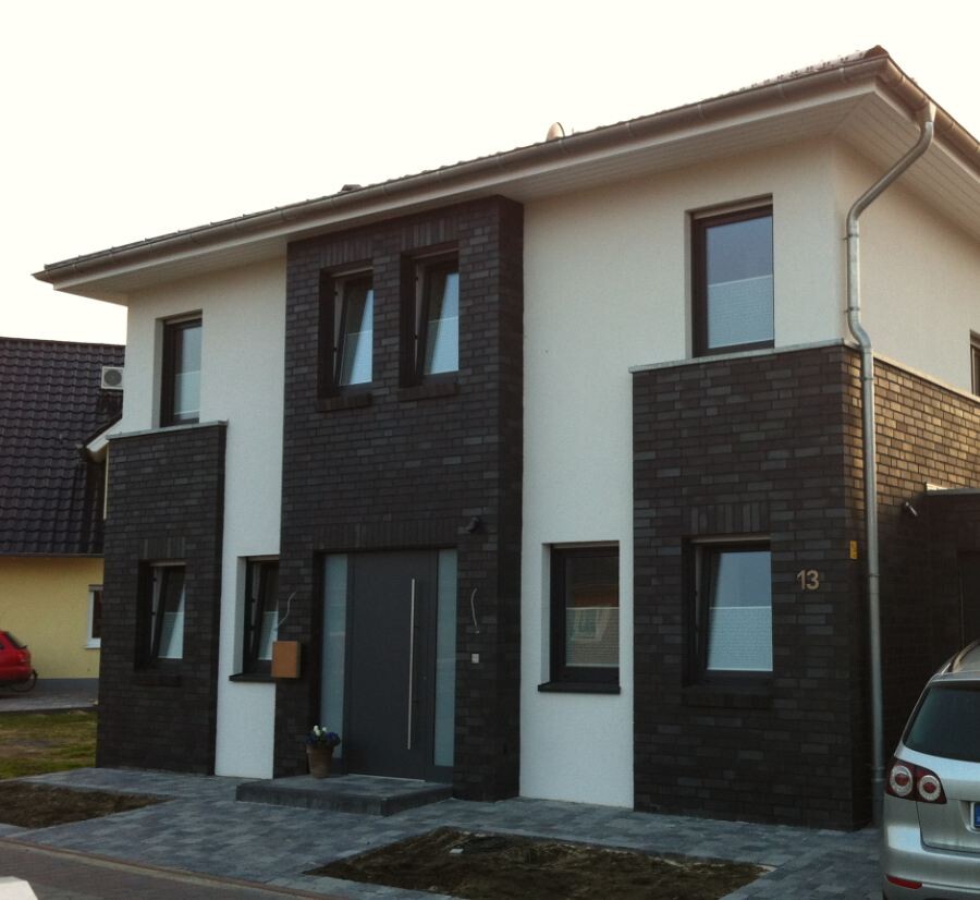 Modern two-story house with white facade, dark brick cladding, and a parked car.