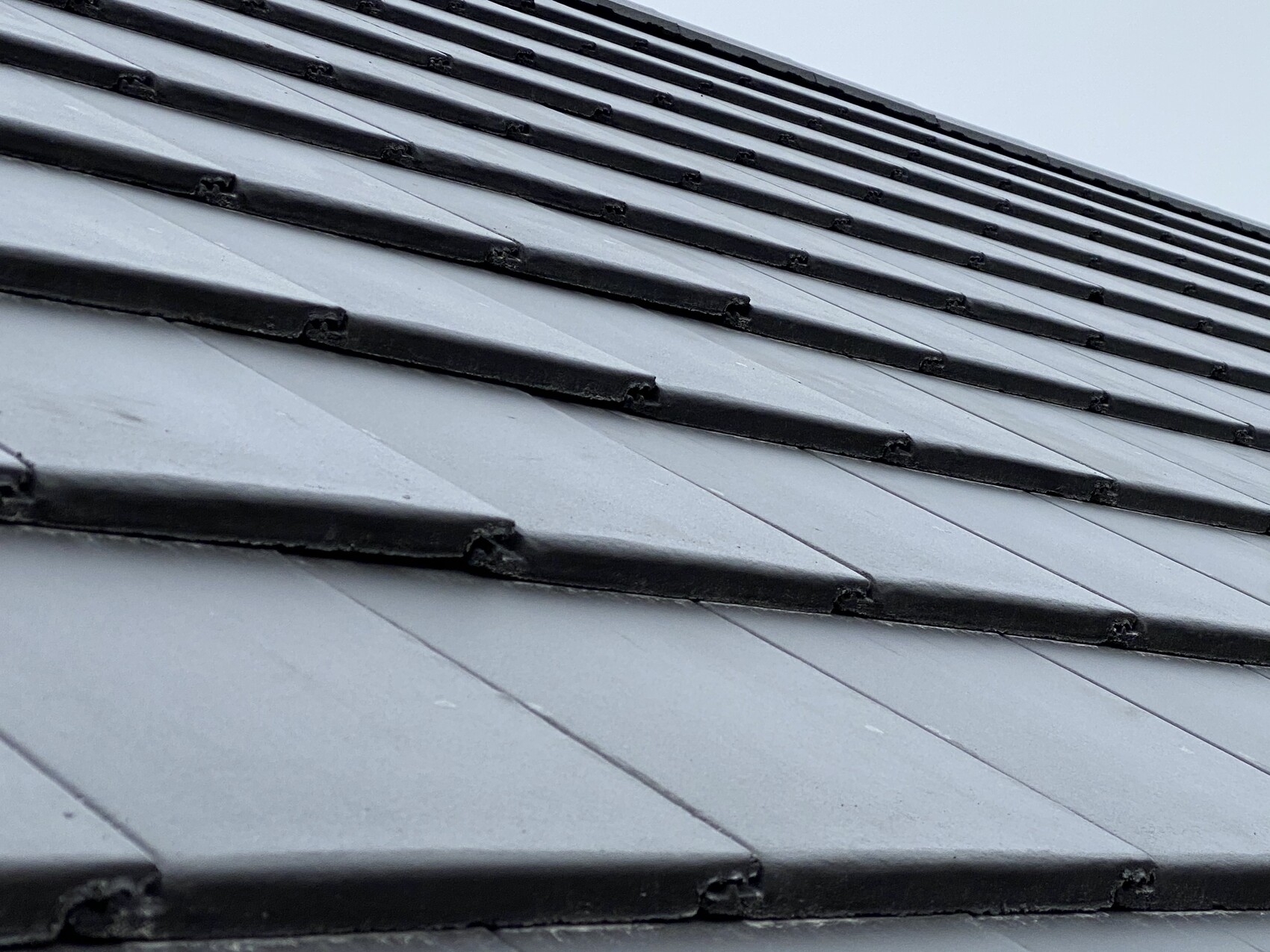 Roof with dark gray, overlapping metal tiles arranged in rows.