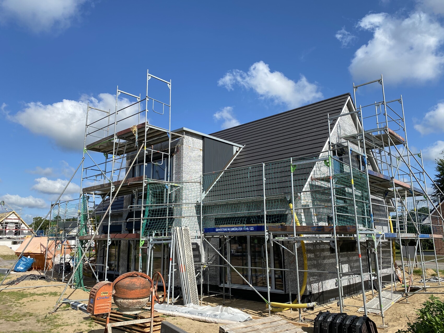 Multi-story house under construction with scaffolding, building materials in the yard, blue sky.