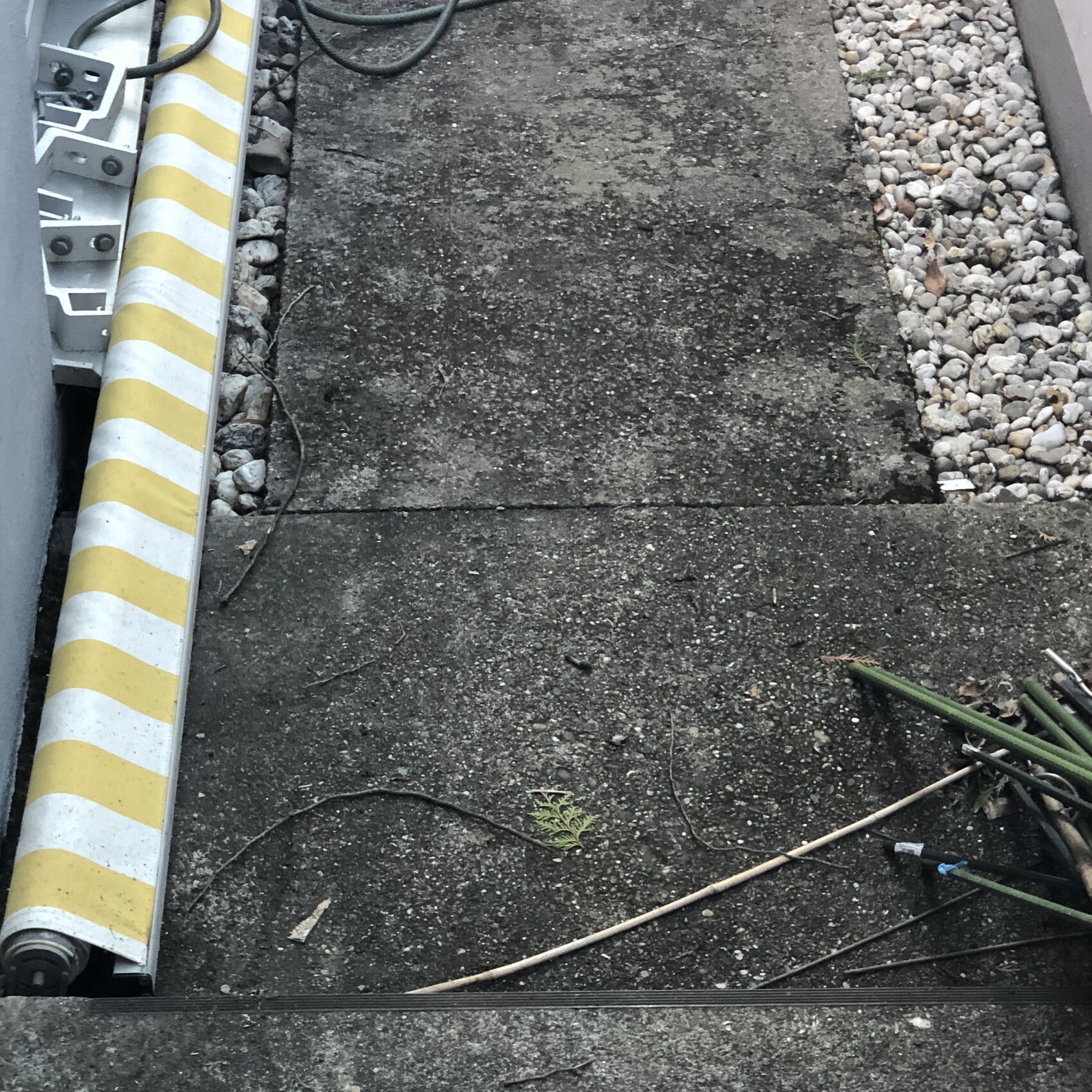 Gelb-weiß gestreifte Baurolle neben Betonplatten, Kabeln, Kies und einer Pflanze zwischen Ritzen.