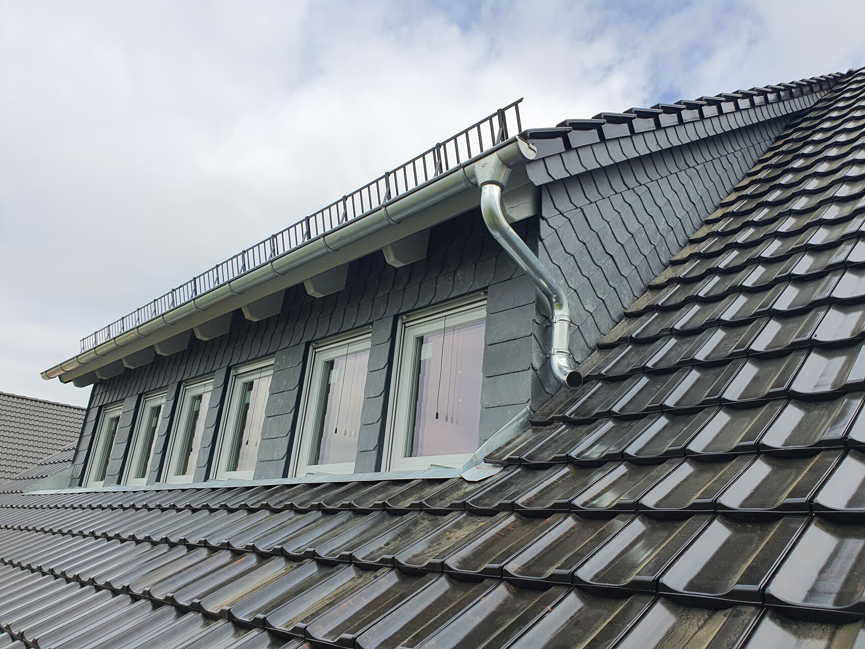 Roof with dark gray tiles, dormer windows, metal gutter and downspout.