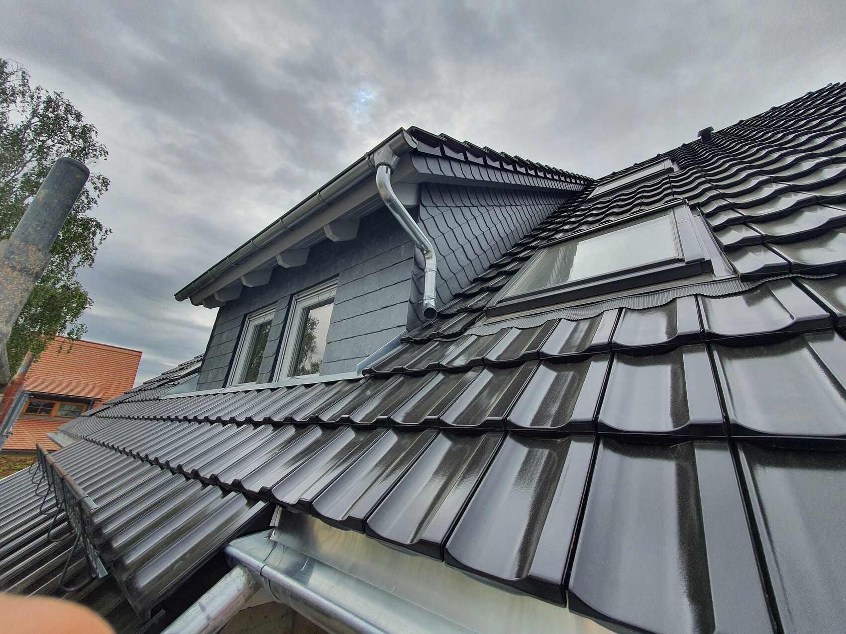 Roof of a house with black, glossy, wavy roof tiles, gutter and dormer window.