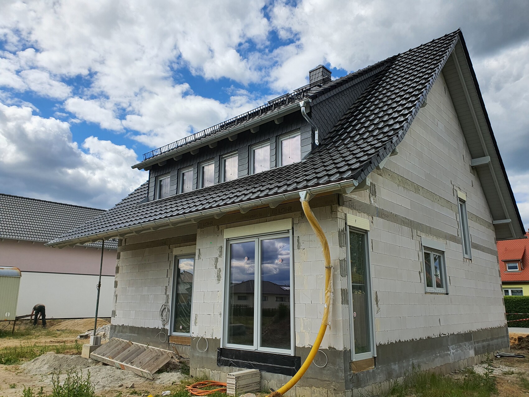 Two-story house in shell construction with gray roof tiles; yellow construction hose on the facade.
