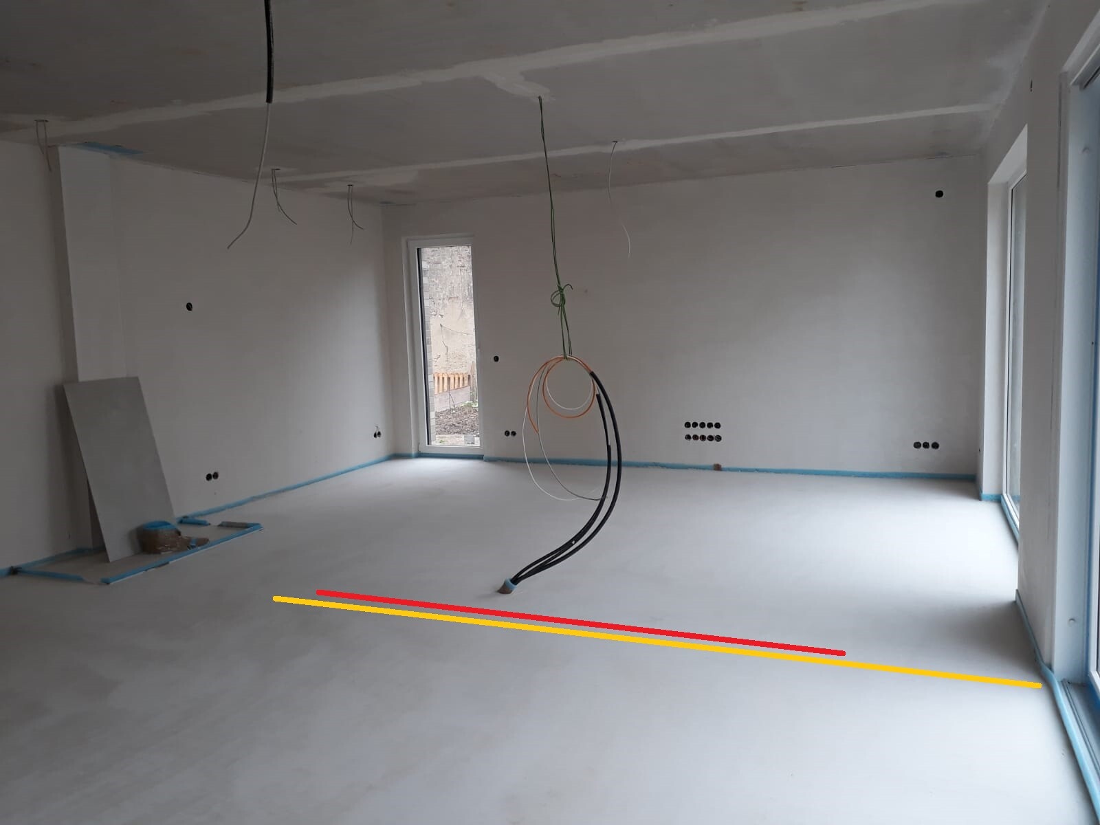 Shell construction room with hanging cables from the ceiling, construction boards on the left, and blue tape on the floor.