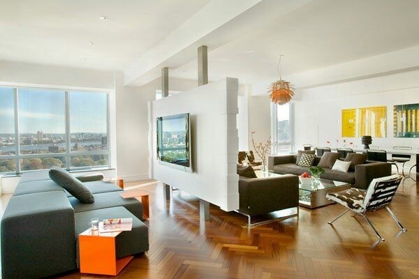 Bright open living space with partition wall, modern furnishings, L-shaped sofas, and city view.