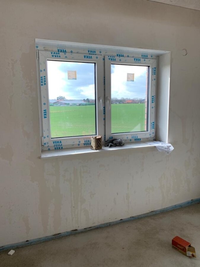 Doppeltes PVC-Fenster in unfertigem Raum; Blick ins grüne Feld außerhalb.