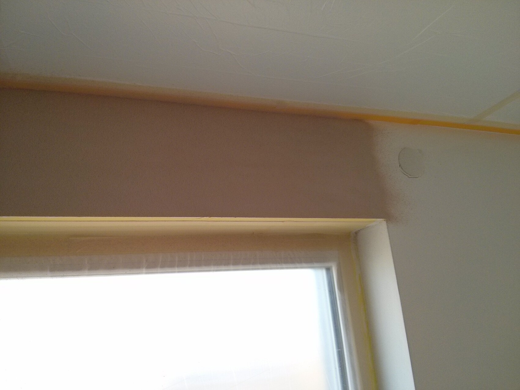 Interior with window below; brown wall stripe and round repair patch; painter’s tape along ceiling edge.