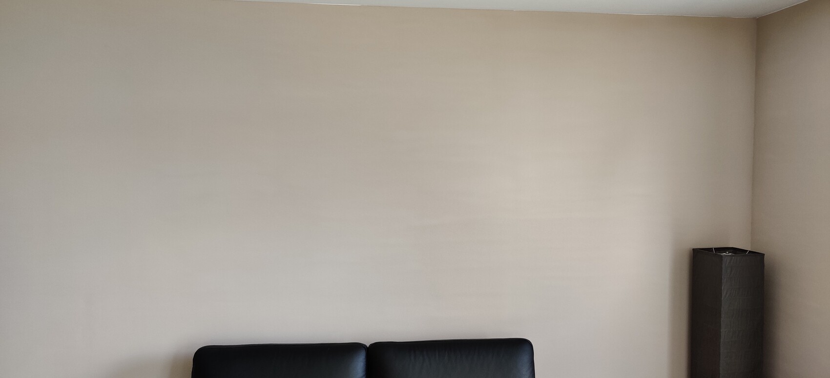 Beige wall with black leather sofa at the bottom; dark rectangular trash bin on the right.