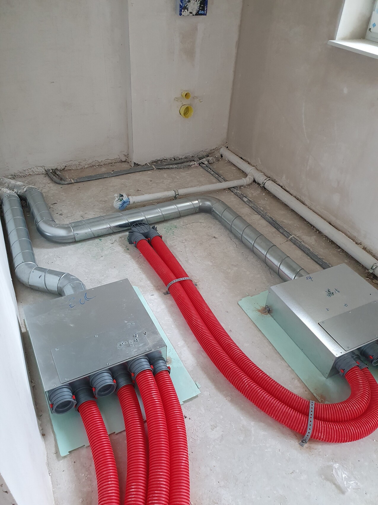 Construction site with open installations: red cable ducts leading to metal distribution boxes, gray pipes.