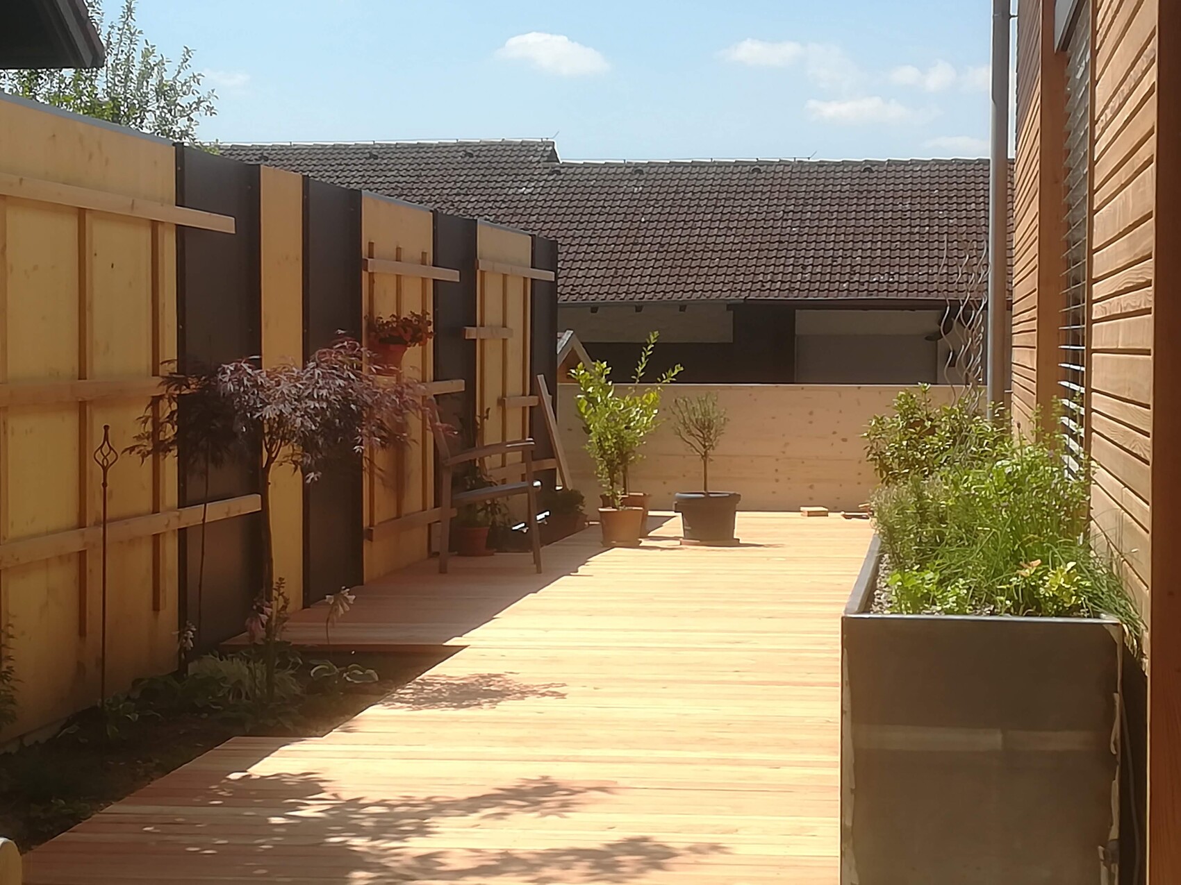 Wooden deck in the courtyard with planter boxes, ladder on the left fence, and side wooden walls.