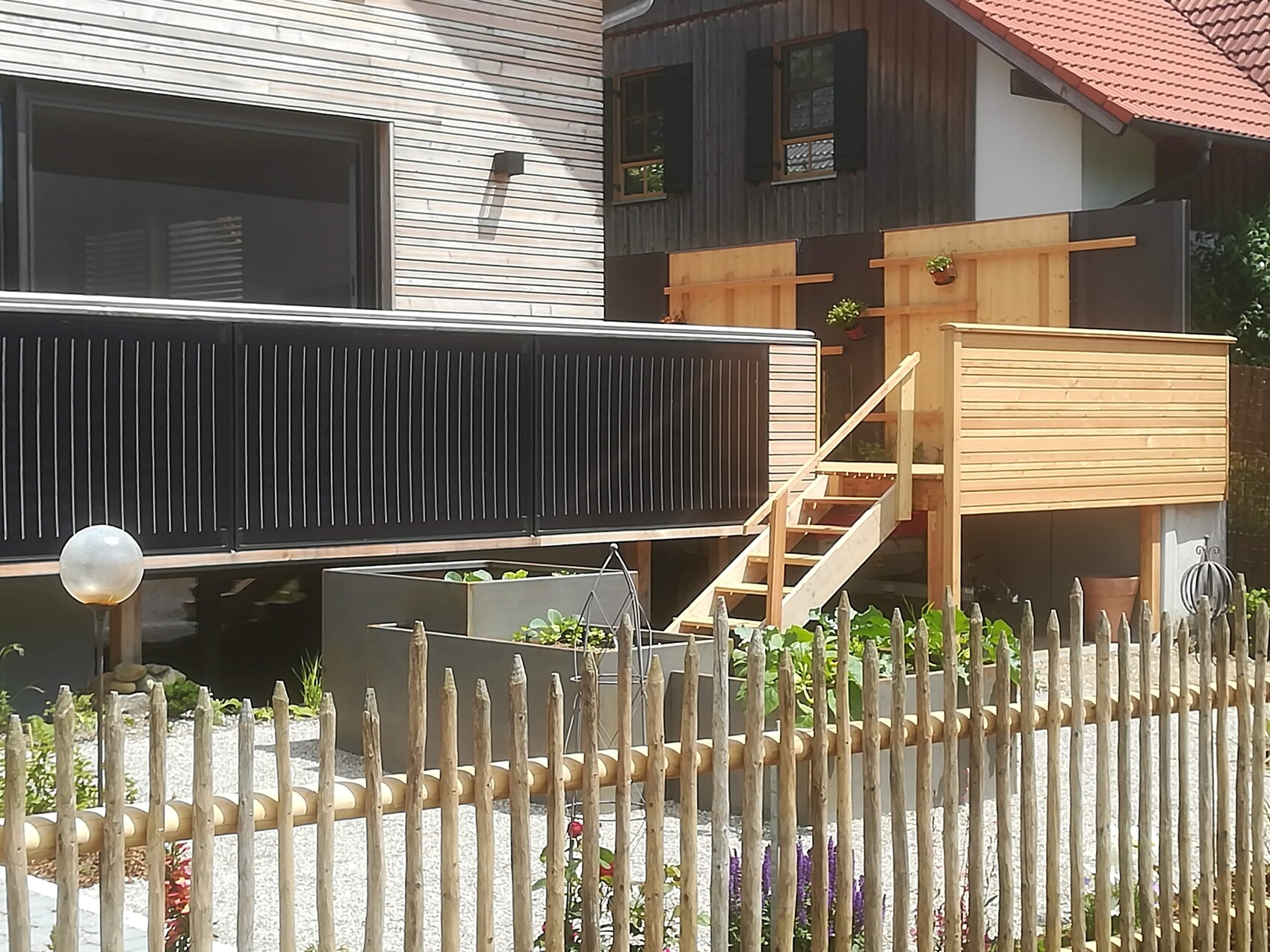 Exterior view of a house with black railing, wooden deck, stairs, and raised wooden garden shed.