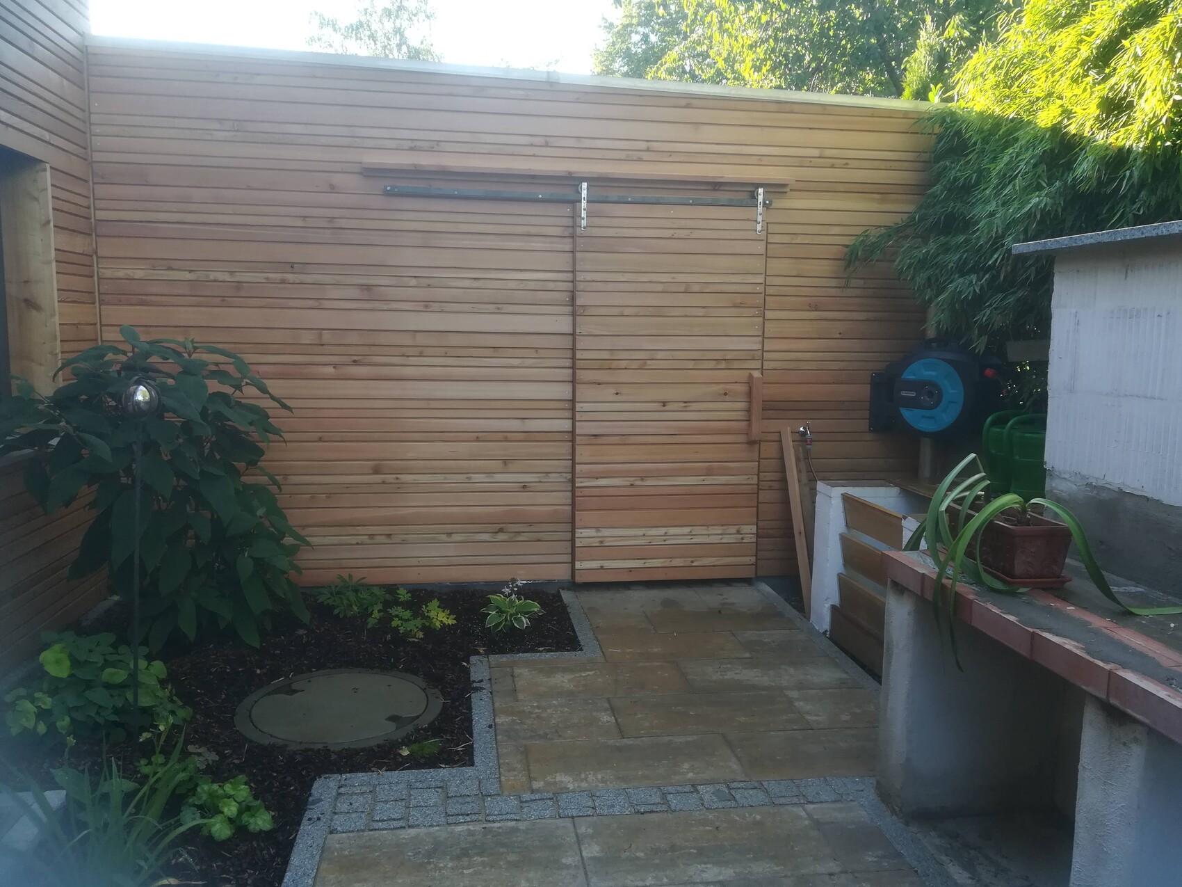 Garden area with wooden slat wall, plant on the left, water tap, hose reel on the right.