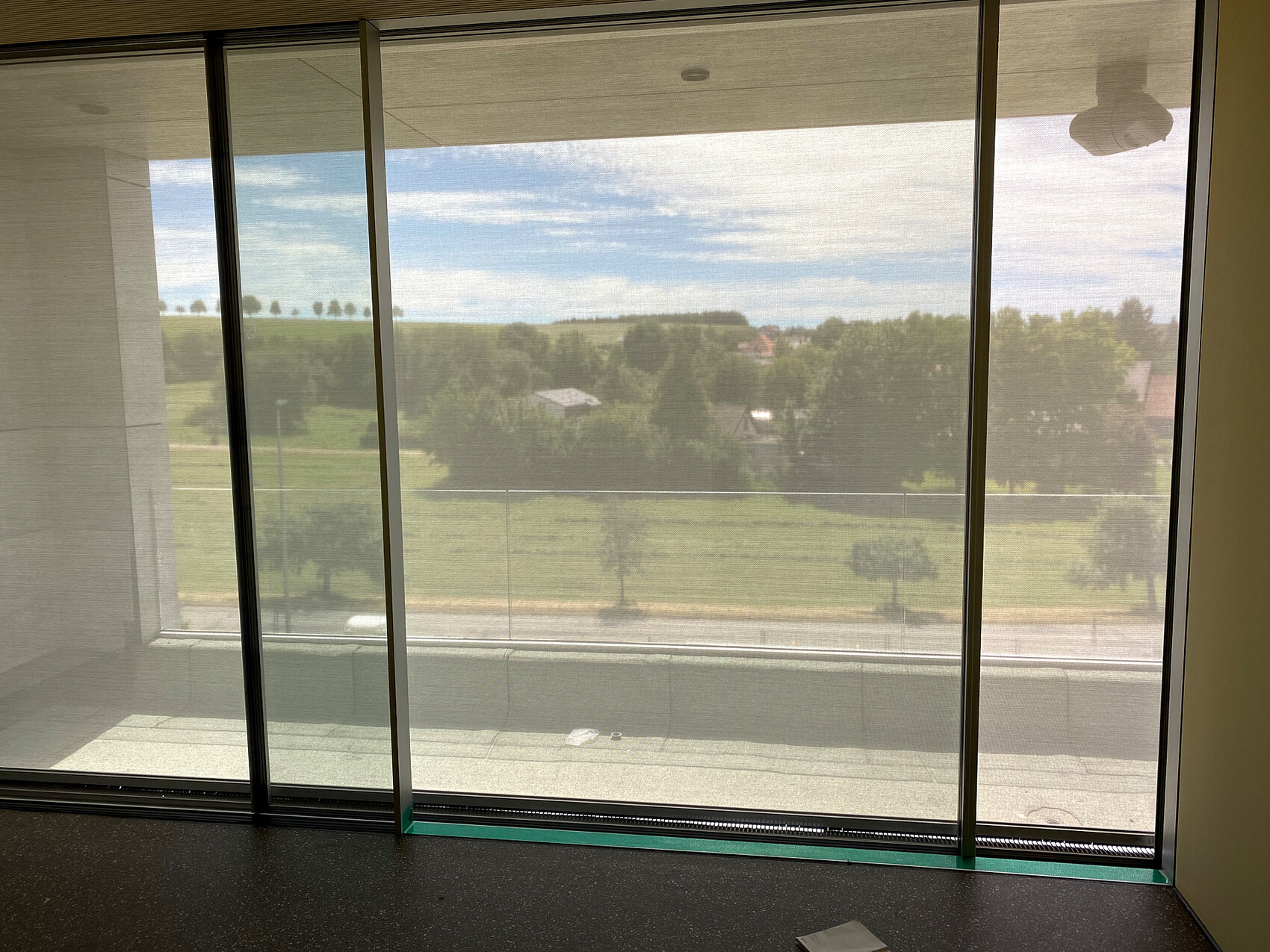 Large glass window: view of green fields, trees and blue sky; interior with bright walls.